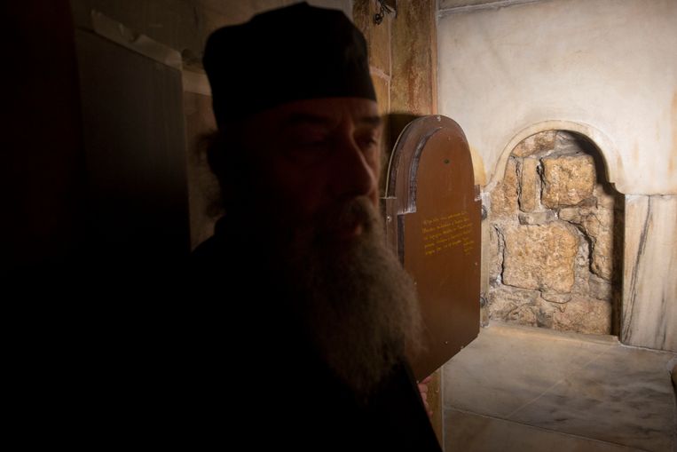 Een Griekse priester bij een raam dat uitgeeft op de binnenkant van de graftombe van Jezus. Het zou een deel van de originele stenen muur zijn van de tombe. 